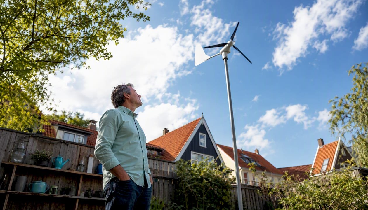 Een man staat in zijn achtertuin bij een kleine windmolen, midden in een woonwijk.